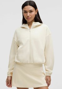 Felpa corta color crema con zip frontale e cappuccio, abbinata a una mini gonna coordinata. Tessuto morbido e vestibilità rilassata per il massimo comfort.