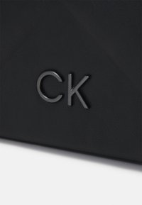 Musta teksturoitu nahkalaukku, jossa kiiltävä hopeanvärinen "CK"-logo. Muotoilu on selkeälinjainen ja rakenteeltaan jämäkkä.