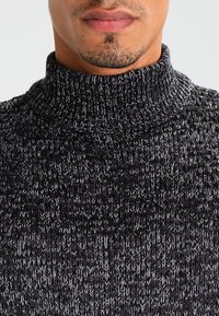 Sweter z golfem wykonany z dzianiny w ciemnoszarym kolorze z jasnoszarymi flekami, z wyraźnym wzorem i dopasowanym krojem przy szyi.