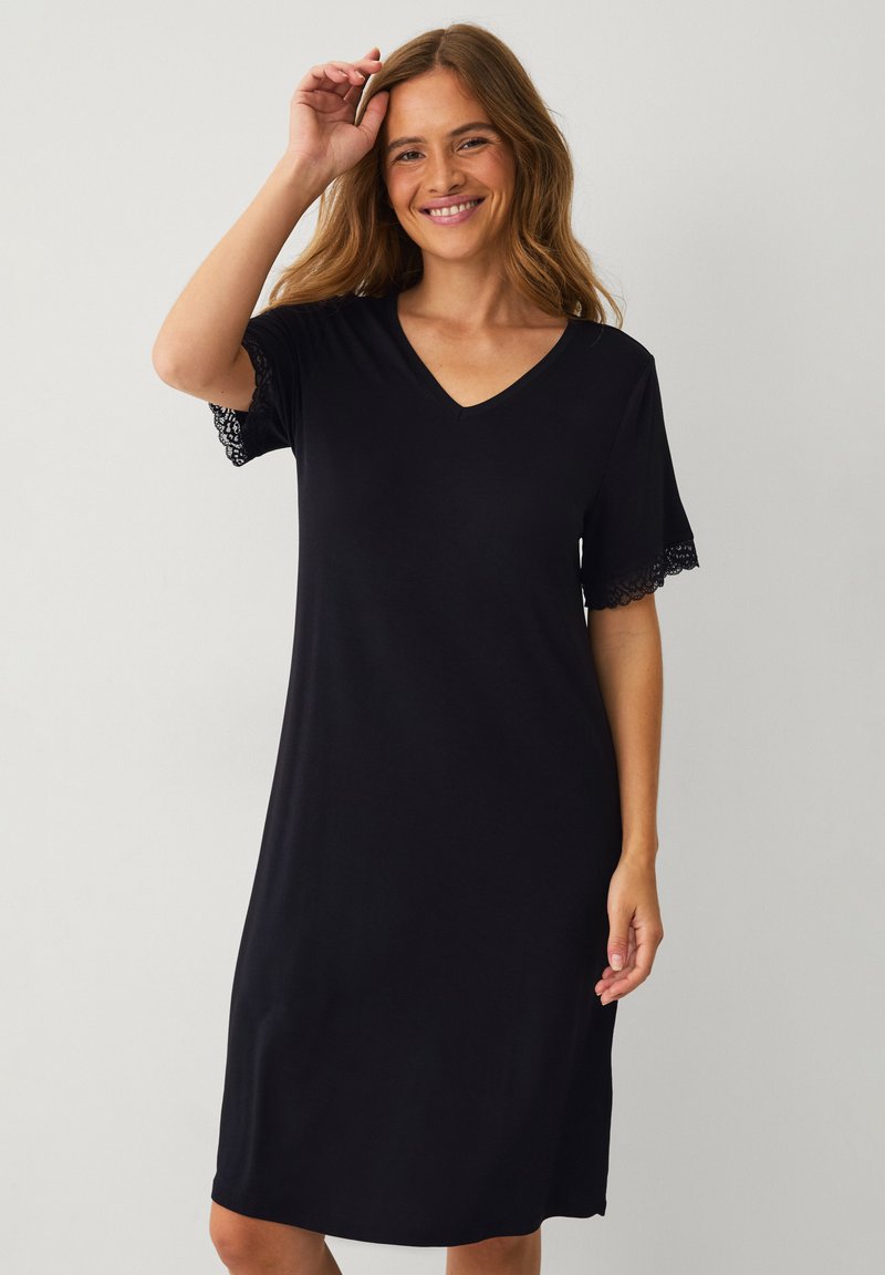 Czarna sukienka z dekoltem w serek i krótkimi rękawami, z koronkowymi akcentami na brzegach rękawów. Miękka tkanina o luźnym kroju, sięgająca do połowy łydki.