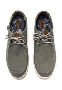 Zapatillas de lona gris con una superficie texturizada, suelas blancas en contraste y plantillas de diseño azul. Presentan cordones grises y acentos marrones.