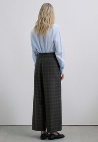Pantalones de cuadros grises de pierna ancha con cintura elástica, combinados con una camisa de manga larga azul claro y zapatos planos negros.