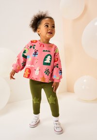 Roza dolg rokav pulover z prazničnimi vzorci; zelene pajkice z apliciranimi filcanimi zvezdami. Bele superge z ježki.