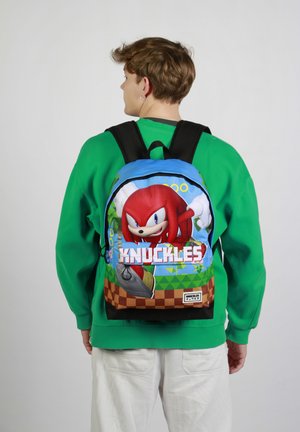 Mochila con Knuckles de Sonic the Hedgehog, predominantemente azul con acentos en rojo, verde y marrón. Hecha de tela con estampados gráficos.