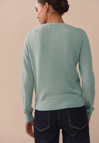 Lichtblauwe kasjmiertrui met geribbelde manchetten en zoom, voorzien van een klassieke ronde hals en subtiele textuur, gecombineerd met donkere spijkerbroek.