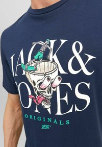 Camiseta azul marino con un gráfico que presenta a un esqueleto patinador sobre un cráneo, con acentos de colores brillantes y un diseño de texto en negrita.