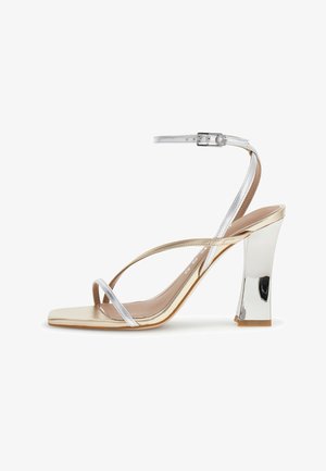 Pumps mit Absatz, metallic-goldener Sohle, silbernen dünnen Riemchen über den Zehen und dem Knöchel sowie einem silbernen Blockabsatz.