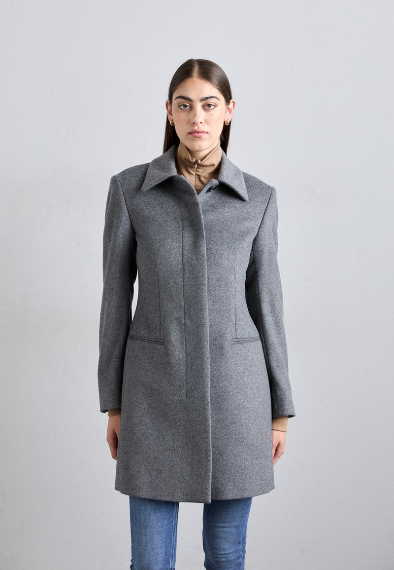 Gray wool coat with a structured design, sharp collar, concealed front closure, and vertical seam details. Worn over a brown top.