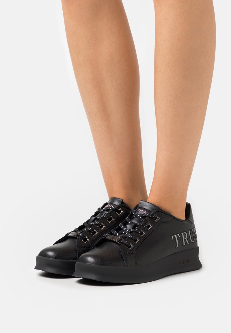 Schwarze synthetische Sneakers mit glatter Oberfl�äche, runden Schnürsenkeln, geprägtem "TRUE"-Branding und einer dicken, strukturierten Sohle.