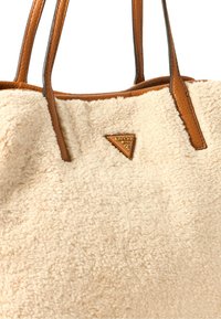 Borsa a spalla in pelliccia sintetica crema con dettagli e manici in pelle marrone, caratterizzata da una spilla a logo triangolare sulla parte frontale. Texture morbida.