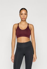 Bordová športová podprsenka s nastaviteľnými ramienkami a okrúhlym výstrihom, v kombinácii s čiernymi legínami s vysokým pásom, ktoré majú hladkú textúru a jemné švové detaily.