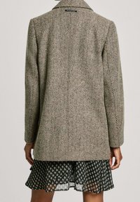 Płaszcz z tweedu w wzór houndstooth w odcieniach brązu i beżu, z klasycznym kołnierzem i długimi rękawami, zestawiony z sukienką w ciemny wzór.