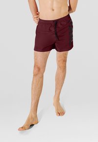 Bañador corto color granate con logo negro en el lateral. Cuenta con una cintura elástica con cordón. Diseñado para ofrecer comodidad y movilidad.