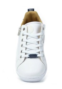 Zapatilla blanca con parte superior de cuero texturizado, cordones blancos planos, cremallera lateral y forro interior marrón. Presenta un logo circular en la lengüeta.