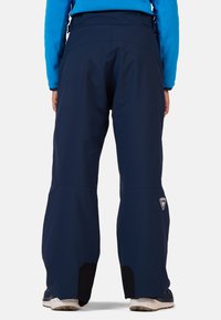 Tummansiniset lasketteluhousut rentoa istuvuutta, valmistettu vettä hylkivästä materiaalista, joissa on vahvistetut lahkeet ja logo-aksentti reidessä.