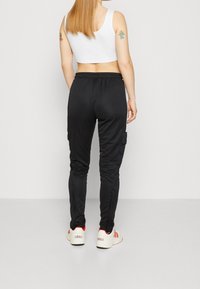 Svarta joggingbyxor med en figurnära design, elastisk midja, sidofickor och avslutade anklar. Kombinationen med vita skor med röda accenter.