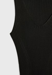Débardeur noir en tricot côtelé avec un col en V et des détails de coutures courbes, fabriqué dans un tissu extensible pour une coupe ajustée.