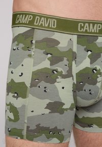 Green camouflage boxer briefs with a knitted waistband labeled "CAMP DAVID." Made of soft fabric, featuring a mix of dark and light green patterns.