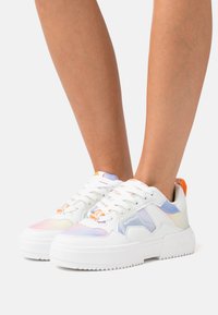 Witte sneakers met een chunky zool, voorzien van pastelaccenten in lavendel, oranje en blauw, evenals vetersluiting en merkteken.