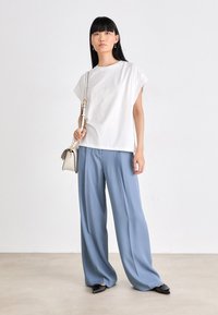 T-shirt oversize en coton blanc à manches courtes, associé à un pantalon large bleu clair. Les accessoires comprennent un petit sac à main blanc et des ballerines noires à bout pointu.