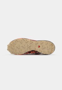 Chaussure de trail running avec une tige noire et orange, dotée d'une semelle en caoutchouc texturé avec des crampons multidirectionnels pour une meilleure adhérence.