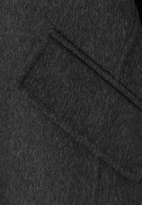 Gros plan d’un tissu en laine gris foncé montrant une poche rectangulaire avec des coutures visibles et une surface douce et texturée.