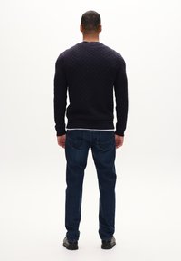 Maglione blu navale a maglia con motivo a diamante testurizzato, polsini e orlo a costine, abbinato a jeans dritti blu scuro e scarpe nere.
