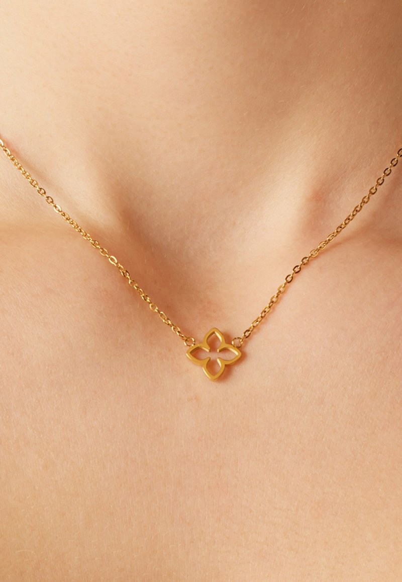 Gouden ketting met een bloemenhanger met uitsnijdingen, bevestigd aan een fijne ketting. Gladde textuur, minimalistisch ontwerp.