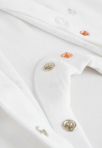 White garment featuring decorative buttons in copper, gold, and silver tones, with a soft, textured cotton fabric.