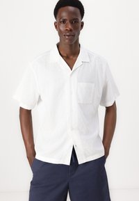 Hvit kortermet skjorte med knapper laget av lett stoff, med et brystlomme og en avslappet krage, kombinert med marineblå shorts.