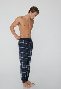 Marineblau karierte Schlafanzughose mit weißen und roten Linien, ausgestattet mit einem Kordelzugbund und tapered Fußbündchen. Weicher Stoff mit Karomuster.