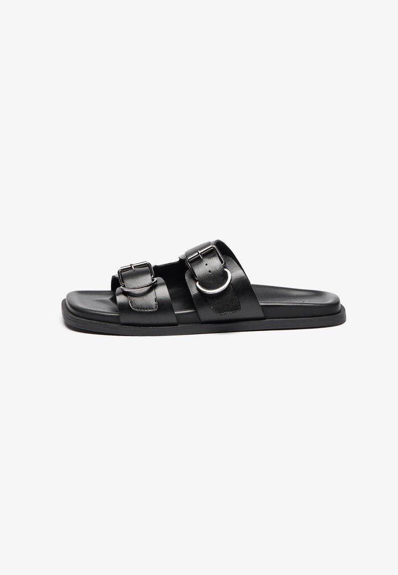 Sandalias planas negras con dos correas ajustables y hebillas plateadas, una suela plana y un acabado mate suave.