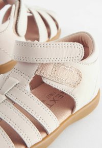 Lichtroze leren sandalen met meerdere horizontale banden, verstelbare klittenbandsluiting en een gestructureerde binnenzool. Bruine rubberen outsole.