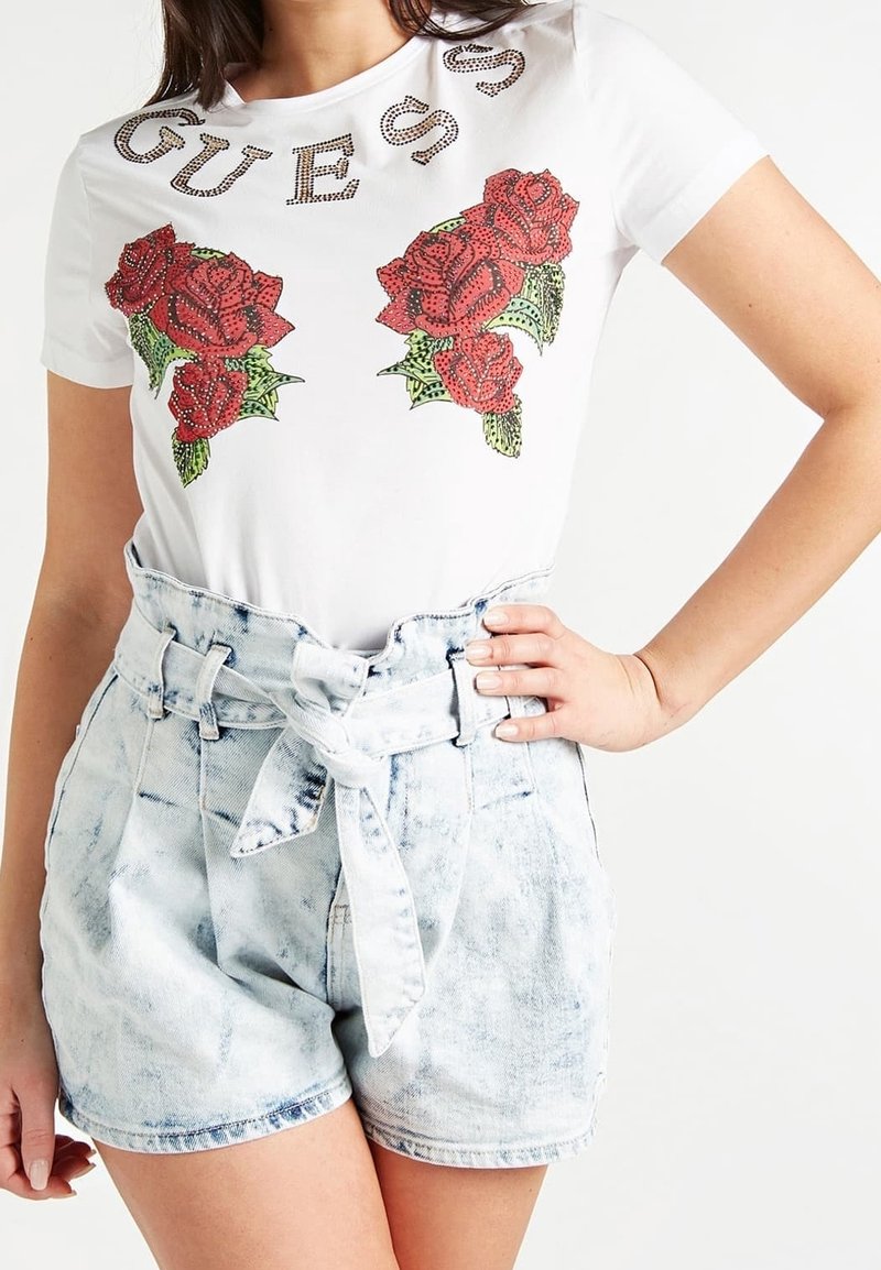 Weißes T-Shirt mit rosem Grafikdesign und Swarovski-Akzenten; kombiniert mit hellblauen Denim-Shorts mit gebundenem Bund und hoher Taille.