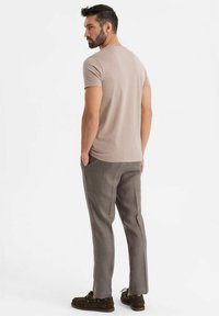 Beige tričko s krátkým rukávem, šedé kalhoty s úzkým střihem a hnědé pohodlné boty. Tento outfit se vyznačuje jednoduchým designem s čistými liniemi a uvolněným střihem.