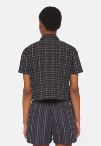 Kurzes kariertes Hemd in Marineblau, Rot und Weiß, mit kurzen Ärmeln, einem Kragen und einem Schlitz hinten. Kombiniert mit passenden karierten Shorts.