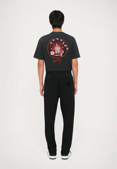 Tricou grafica negru cu un design colorat pe spate, asortat cu pantaloni negri și adidași, evidențiind o croială lejeră.