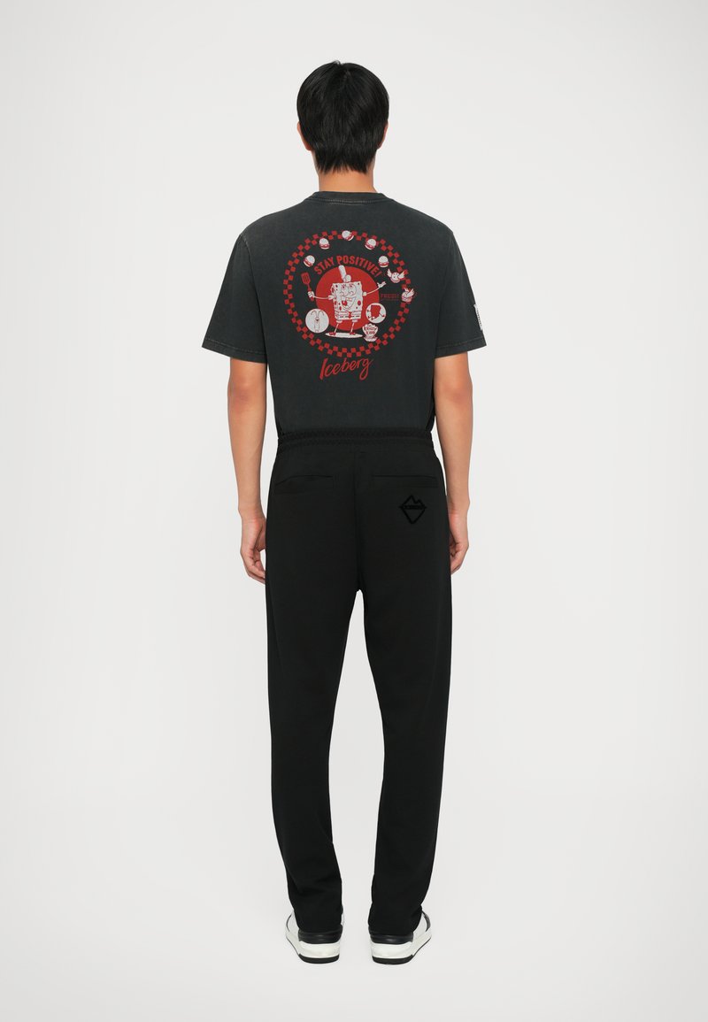 Sort grafisk t-shirt med et farverigt design på ryggen, parret med sorte bukser og sneakers, der viser en afslappet pasform.