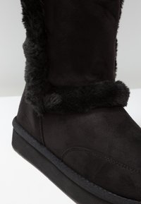 Svart boot gjord av mjuk mocka med en fuskpälskant. Utrustad med en platt gummisula och en slät yta, med fokus på komfort och värme.