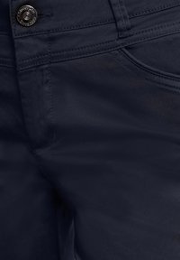 Pantalon bleu marine foncé en gros plan montrant le bouton avant, la ceinture, les coutures et les détails des poches.