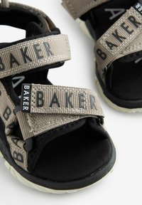 Čierne a béžové sandále s nastaviteľnými textilnými popruhmi s logom "BAKER", textúrovanými materiálmi a polstrovanou čiernou podrážkou.