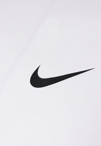 Tissu blanc avec un logo Nike swoosh noir bien visible. La texture est lisse avec un léger éclat, présentant un design minimaliste.
