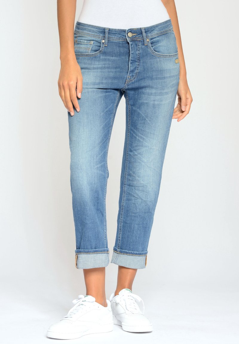 Ljusblå denimjeans med avslappnad passform, uppvikta fållar, fem fickor och detaljer i guldton. Kombineras med vita sneakers.