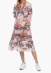 Abito midi floreale in rosa e rosso, con maniche lunghe e colletto. Presenta intricati motivi paisley e un orlo fluente. Indossato con sneakers bianche.