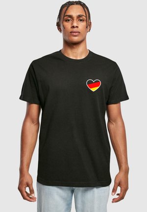 Black cotton t-shirt featuring a heart design with a red, black, and yellow colored flag inside. Short sleeves, crew neck, relaxed fit.