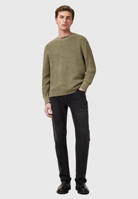 Olijfgroene gebreide trui met een ronde hals, gecombineerd met zwarte slim-fit jeans en zwarte laarzen. Eenvoudig, modern ontwerp met minimale accenten.