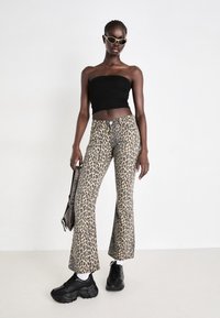 Jeans évasés à imprimé léopard avec une taille haute, associés à un haut tube noir ajusté et des baskets noires chunky. Accessoirisés avec un sac à épaule.