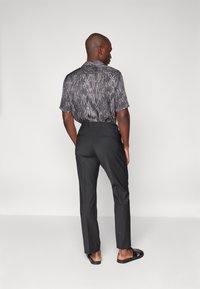 Chemise à manches courtes à motif en peau de serpent noir, associée à un pantalon noir ajusté. Modèle montré de dos, portant des sandales noires.
