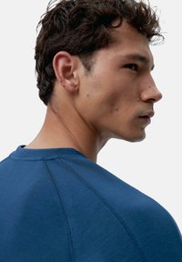 Temno modra kratka majica s kratkimi rokavi in okroglim izrezom, z teksturirano tkanino in vidnimi šivi na rami.