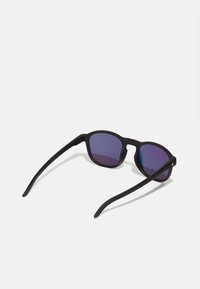 Ochelari de soare cu un cadru negru mat, lentile pătrate care trec de la violet la albastru și brațe subțiri, elegante. Fără logo-uri sau modele vizibile.